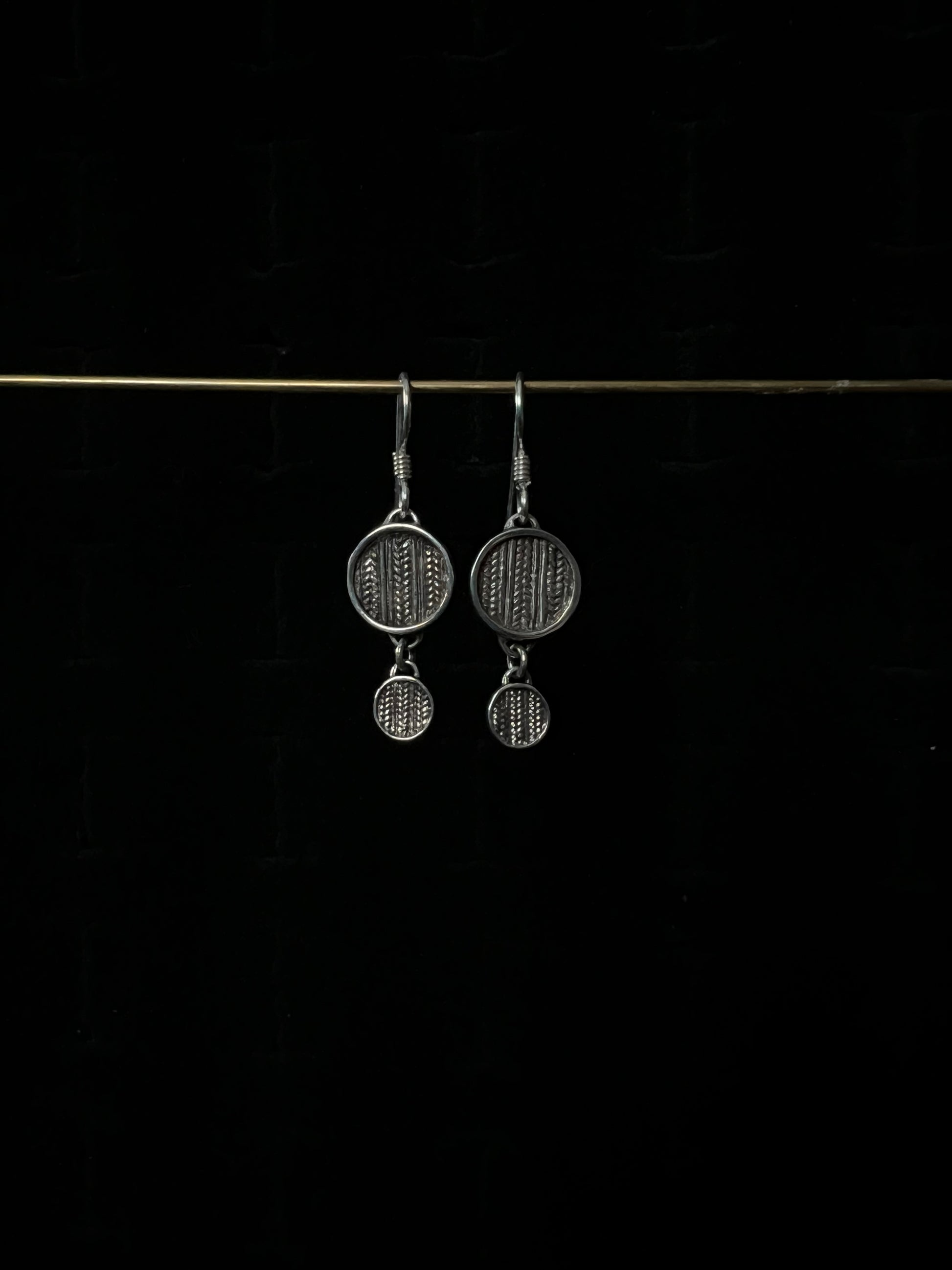 A pair of silver tiered sweater drop earrings displayed against a dark background.