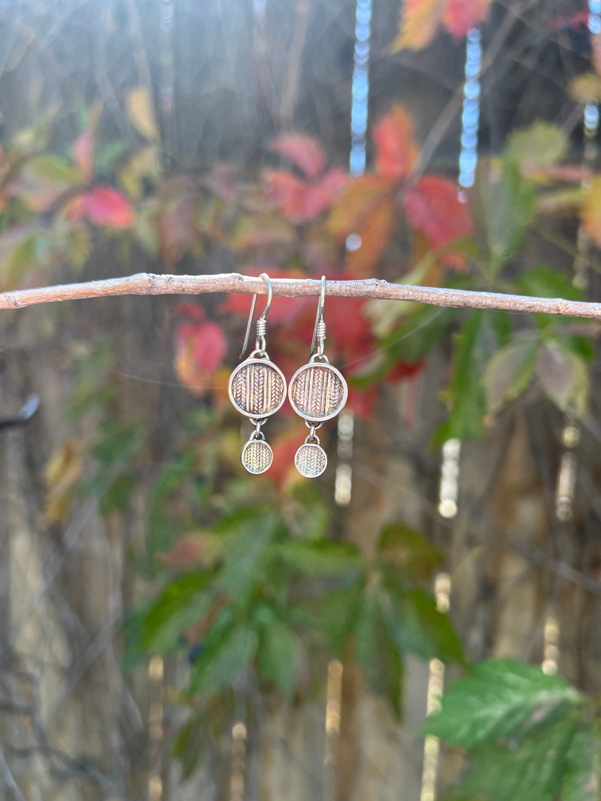 Tiered Sweater Drop Earrings – lifestyle shot of handcrafted sterling silver tiered sweater-texture disc earrings resting on dark knit sweater near fireplace