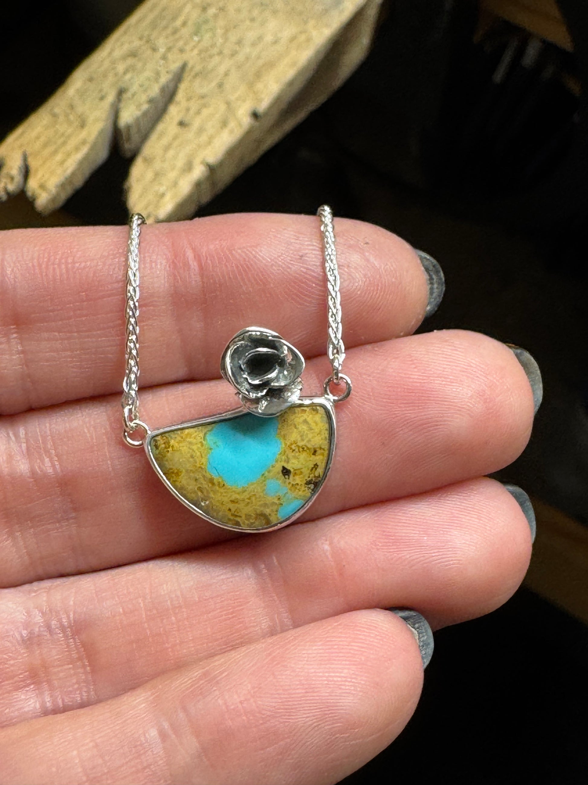 Silver necklace with a heart-shaped pendant featuring blue and gold colors held between fingers.
