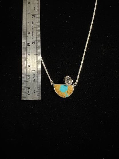 Necklace with a half-circle pendant on a black background, measured against a ruler.