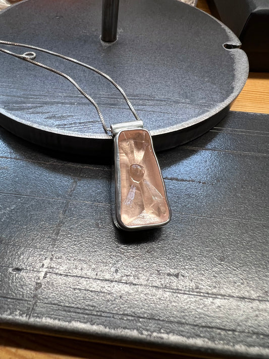 A Vantage Cut Glass pendant in a sterling silver bezel setting, displayed on a textured surface.