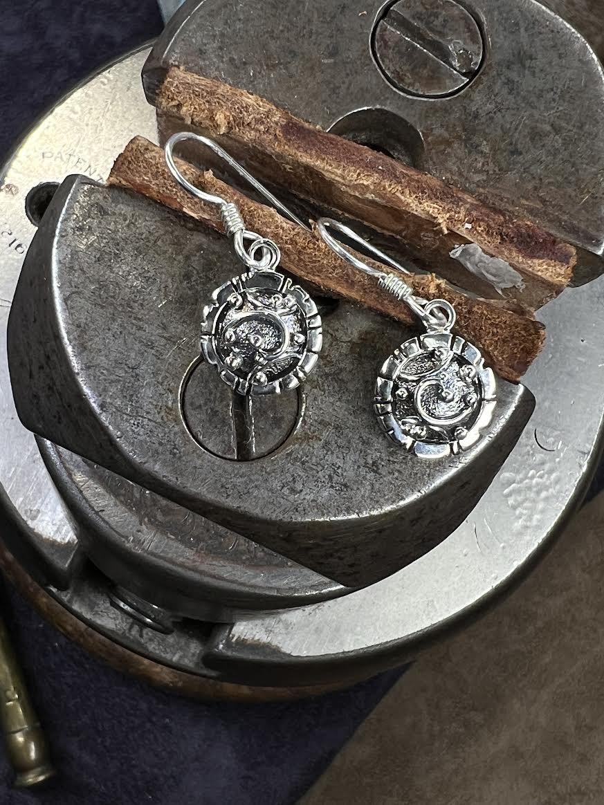 Artisanal Elements Earrings – lifestyle shot of handcrafted sterling silver artisanal disc drop earrings displayed on vintage anvil in worksho