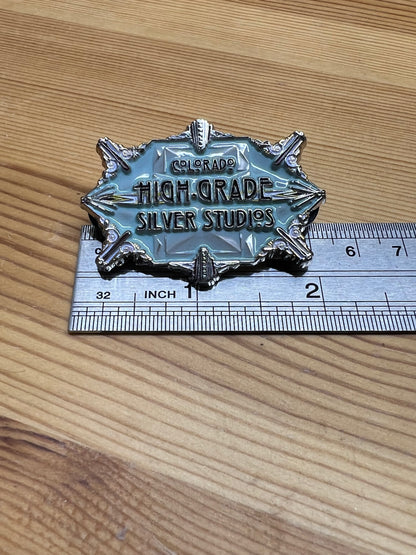 Colorado High-Grade Silver Studios enamel pin – size reference showing large art deco starburst pin approximately 2 inches wide next to ruler, wooden surface