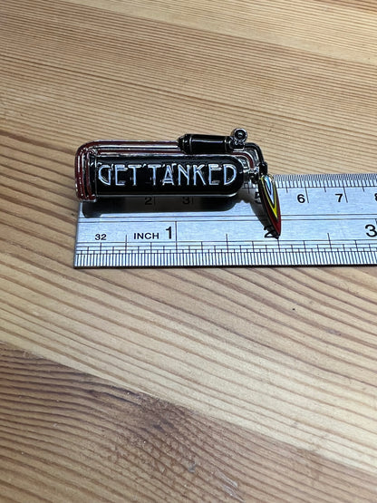 "Get Tanked" enamel pin – horizontal size reference showing pin width approximately 1.5 inches next to ruler, wooden surface