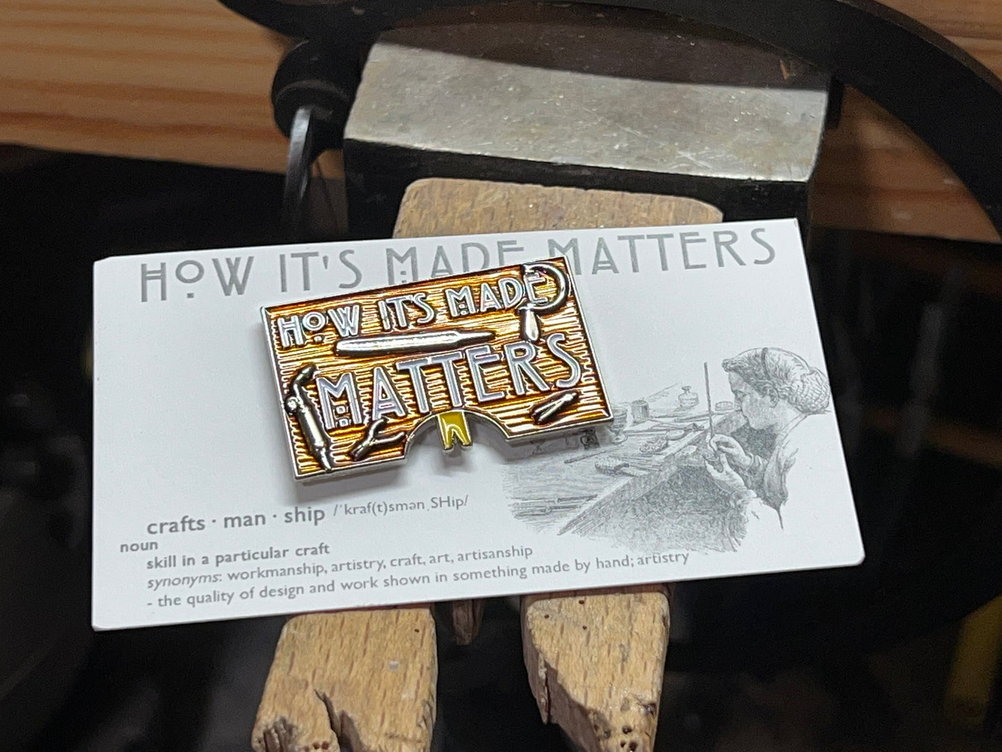 A rectangular enamel pin with a jeweler's bench design and the text 'HOW IT'S MADE MATTERS' on a craftsman's shirt.