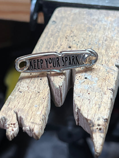"Keep Your Spark" enamel pin – close-up of hard enamel gold and silver torch flame pin with Keep Your Spark lettering, wooden surface