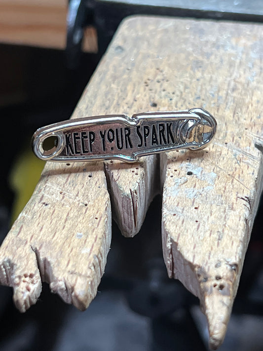 "Keep Your Spark" enamel pin – close-up of hard enamel gold and silver torch flame pin with Keep Your Spark lettering, wooden surface
