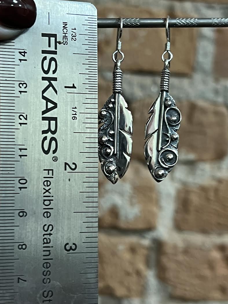 Long Feather Earrings – lifestyle shot of sterling silver long feather drop earrings displayed outdoors on natural surface