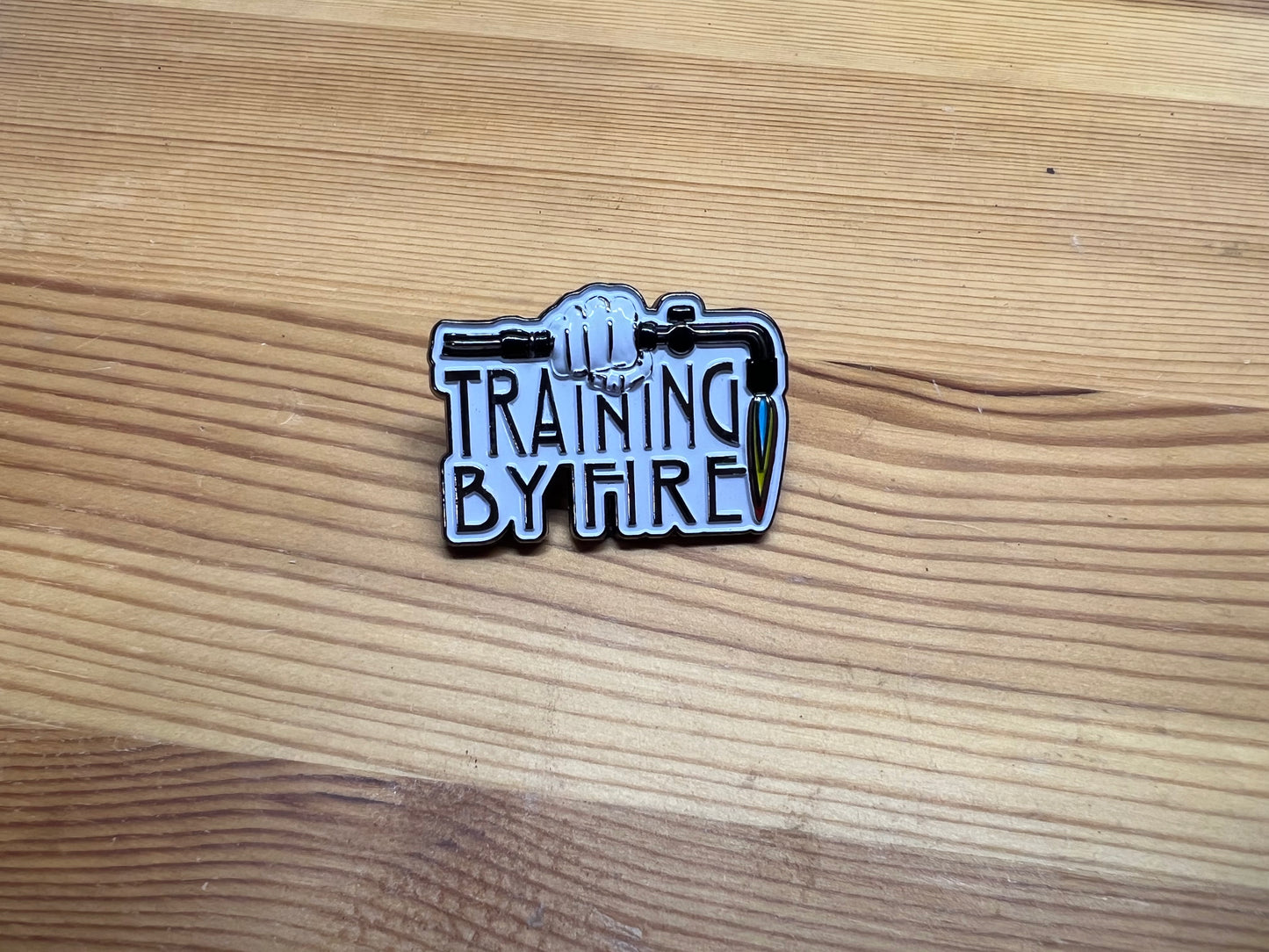"Training By Fire" enamel pin – front view of hard enamel torch pin on white background