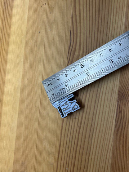 "Training By Fire" enamel pin – back view showing butterfly clasp hardware, wooden surface